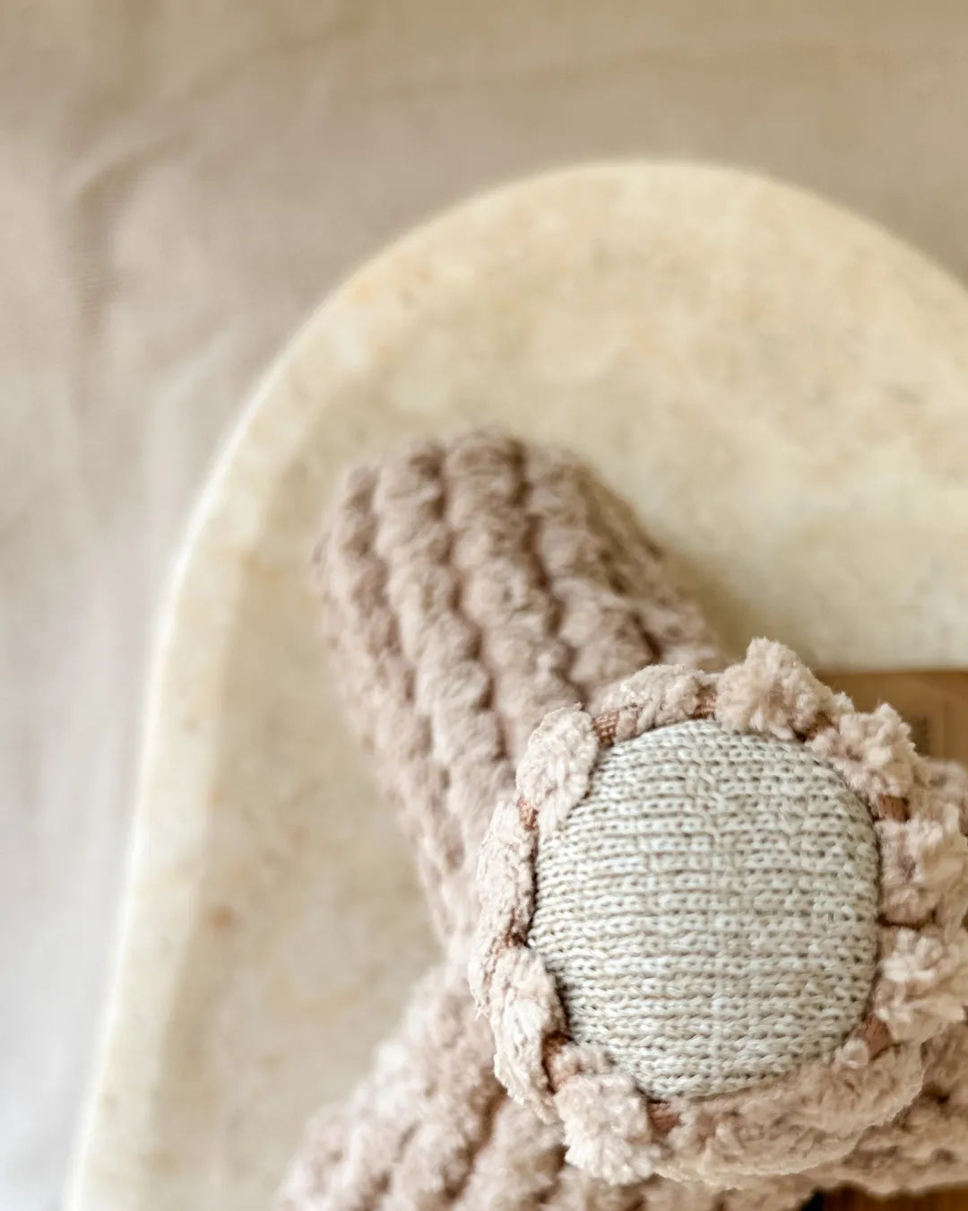 Close-up of a soft textured beige dog toy with a knitted pattern on a neutral background