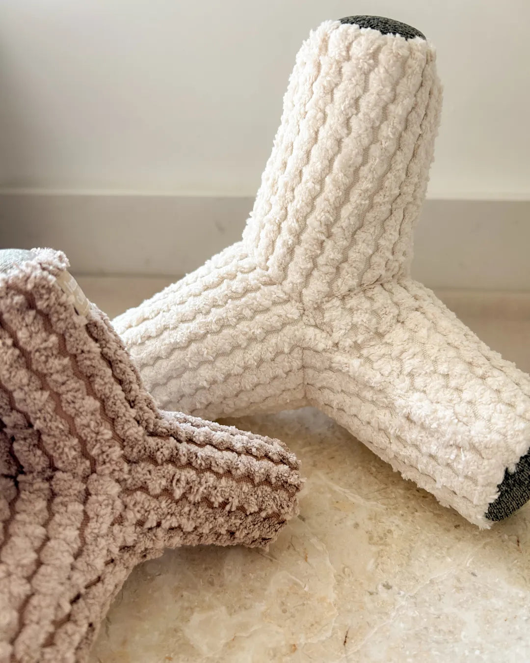 Textured beige and brown dog toys on a light marble floor.