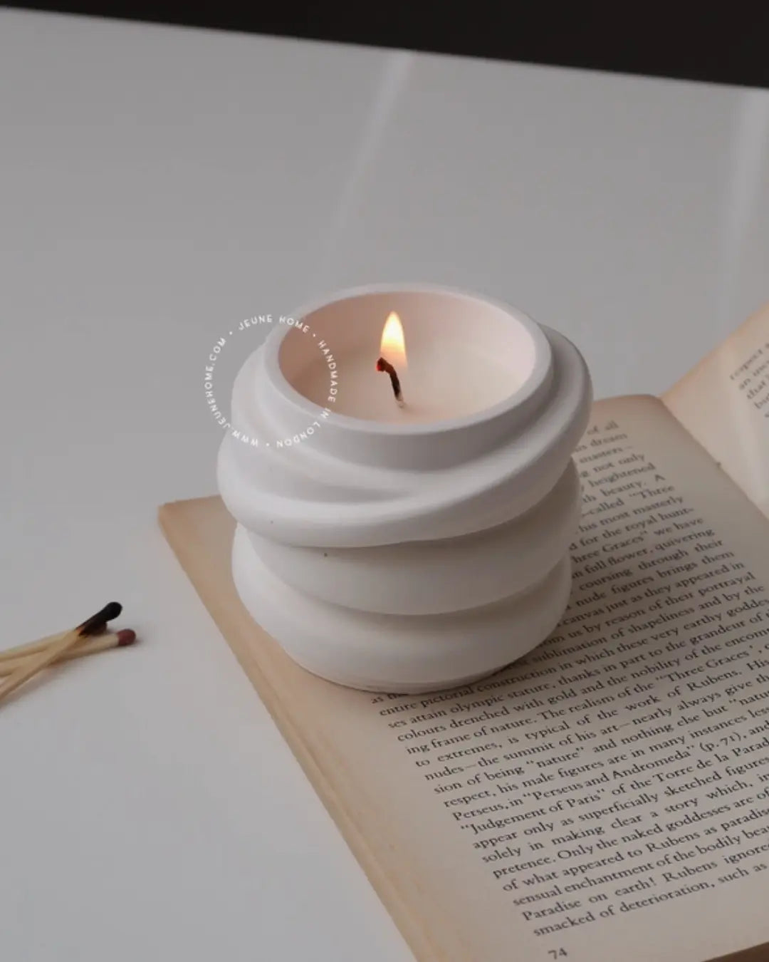 White ceramic candle holder with a lit candle on an open book