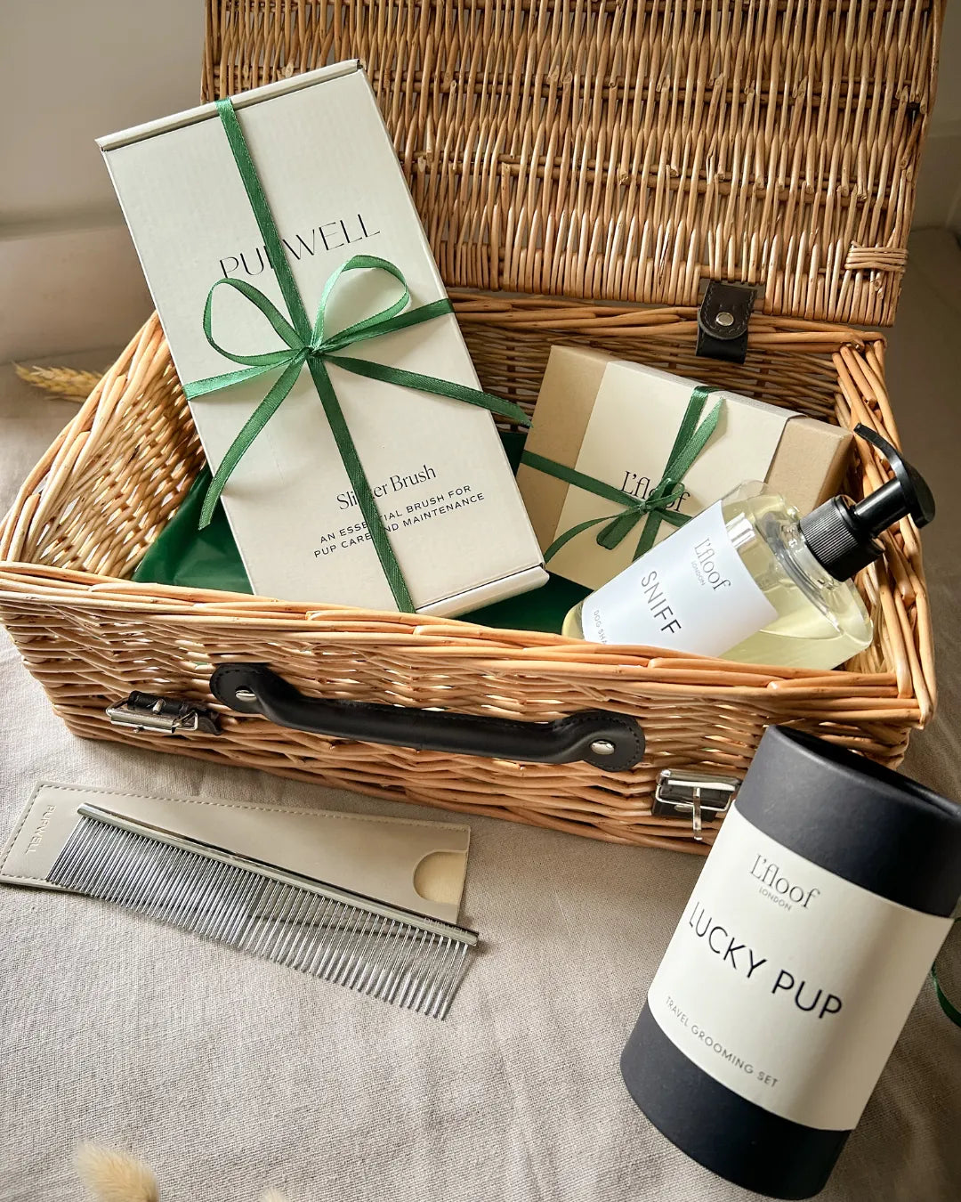 Luxury wicker hamper with pet care products including a slicker brush, dog shampoo and a dog comb on a neutral background.