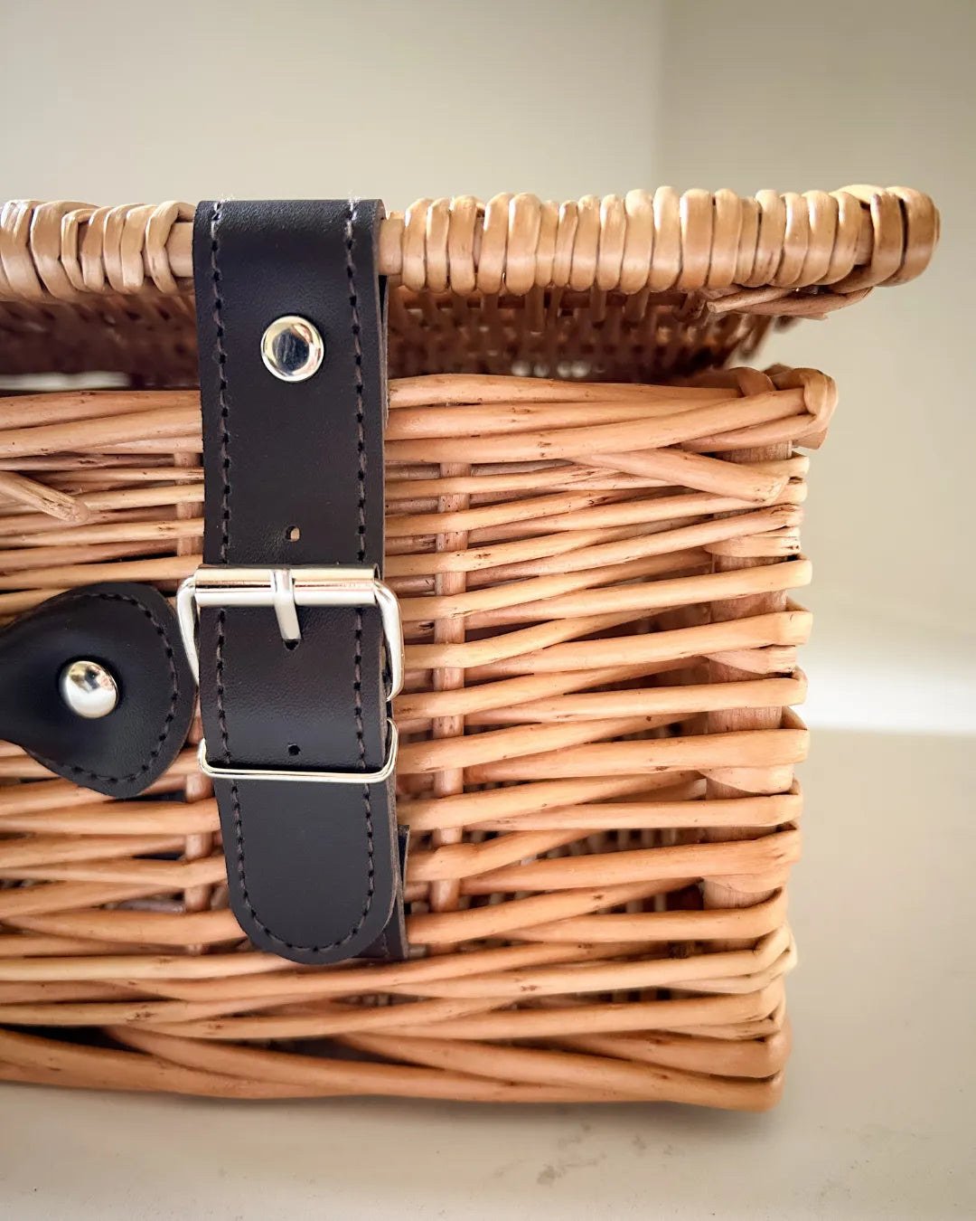 Wicker basket with black vegan leather strap on a light background