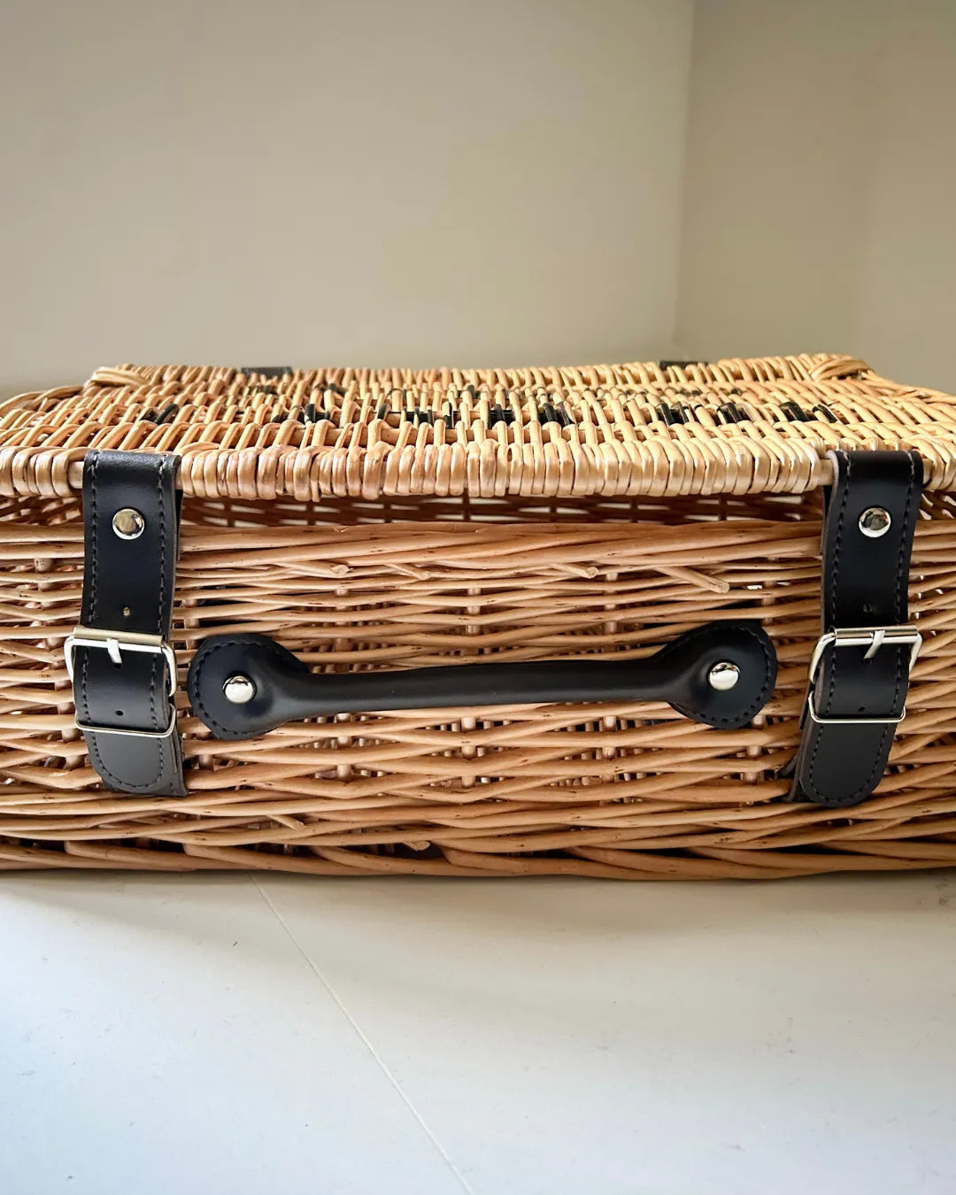 Luxury wicker hamper with black straps on a light background