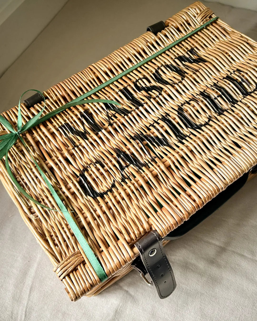 Luxury wicker hamper with a green ribbon and 'Maison Caniche' branding on a neutral background