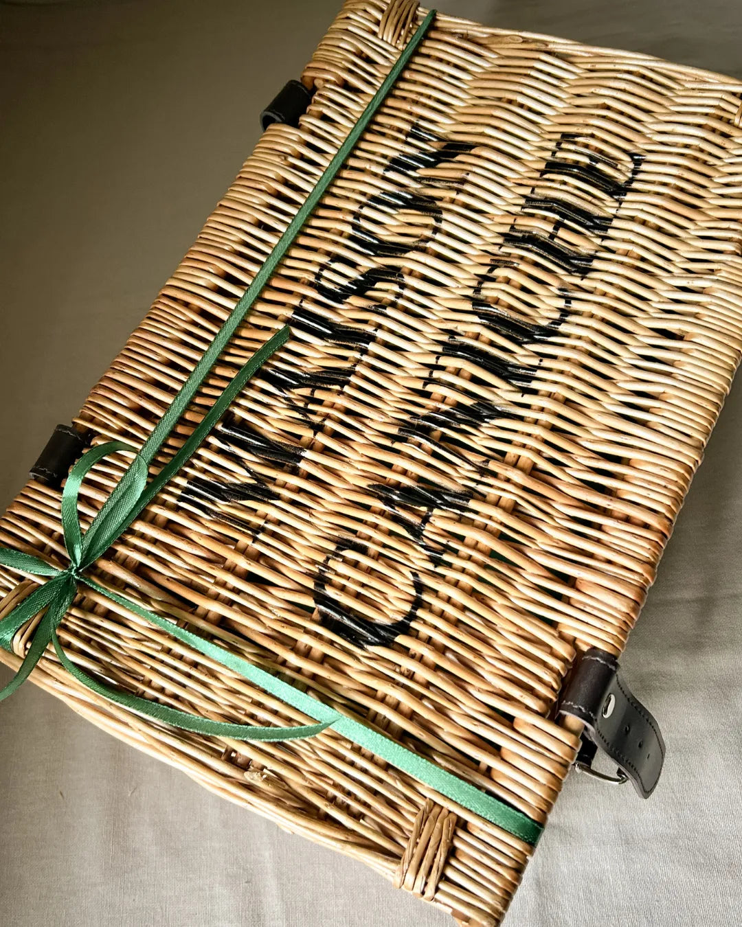 Luxury wicker hamper with a green ribbon on a beige surface