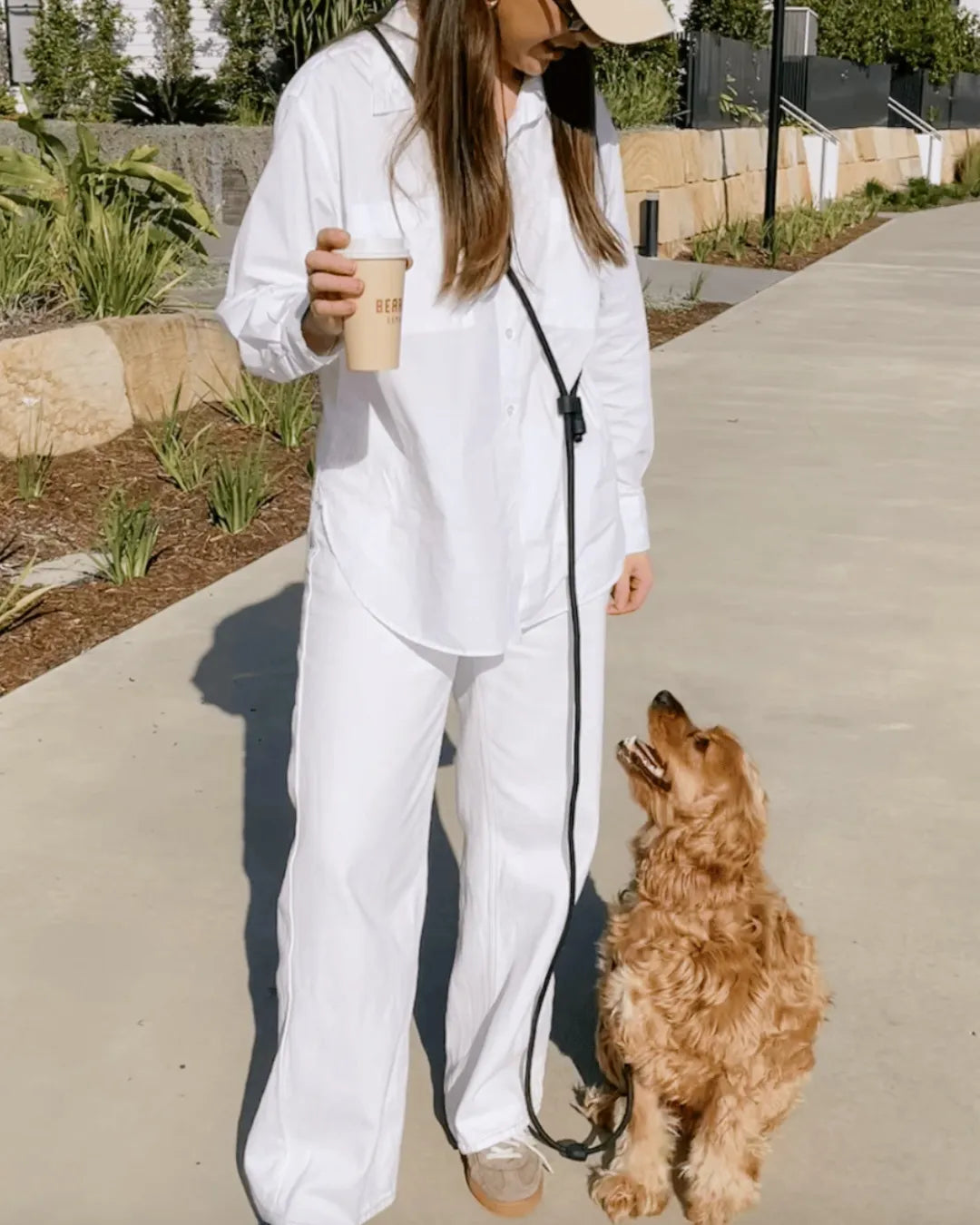 Person in white outfit holding a coffee cup with a dog on a luxury black rope dog lead outdoors