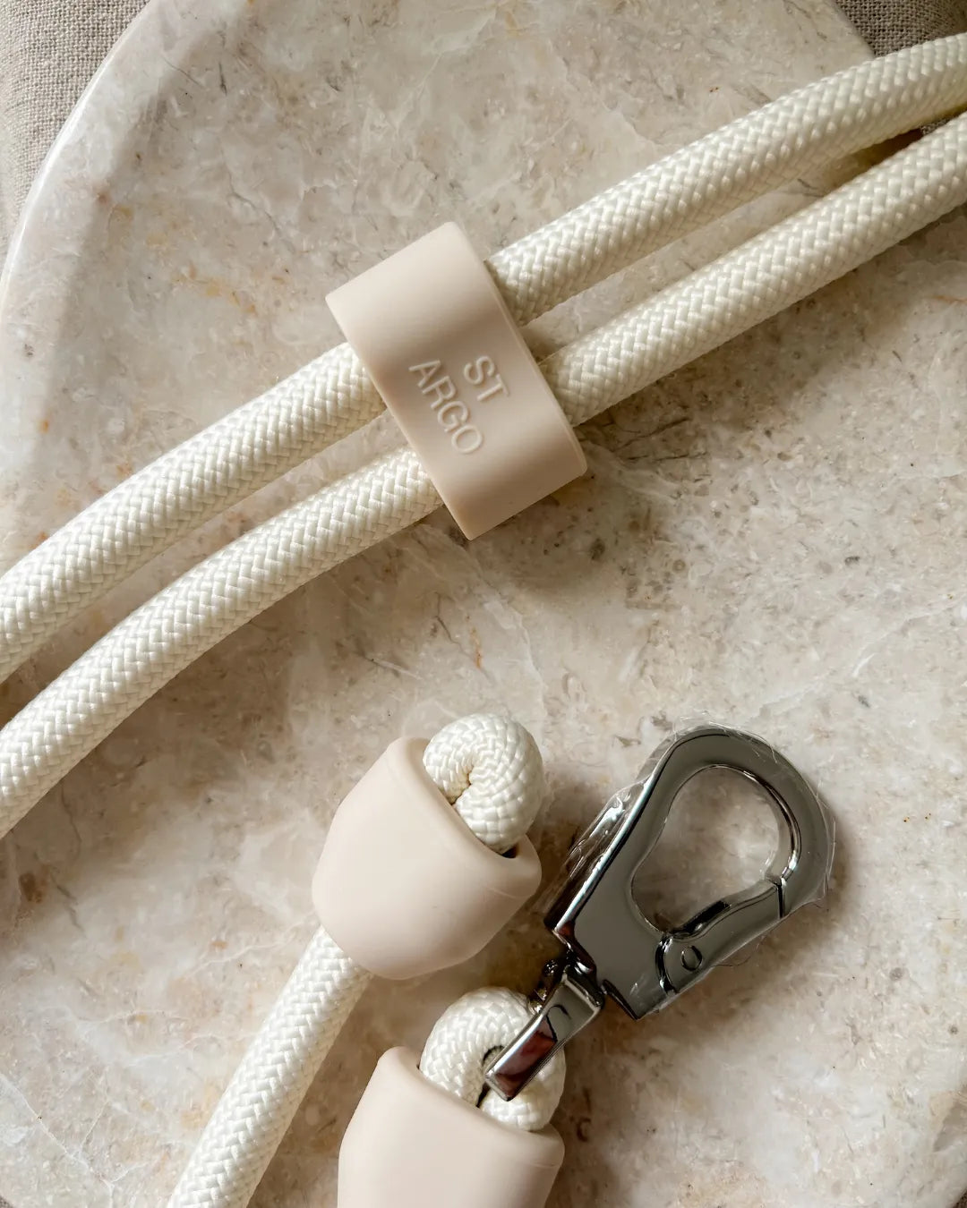 Close-up of a minimalist beige rope handsfree lead with a metal clasp and silicone features on a marble surface