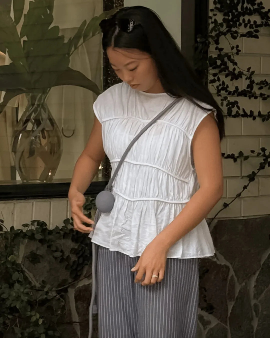 Woman wearing a white blouse and striped trousers standing outdoors with plants in the background and a luxury handsfree dog lead over her shoulder