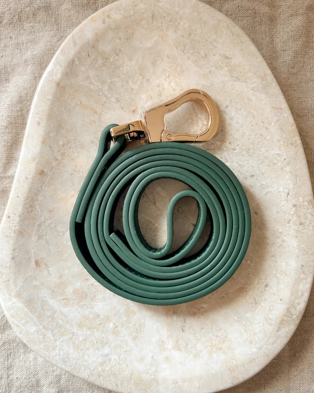 Luxury dark green vegan leather dog lead with a gold clip on a beige stone surface