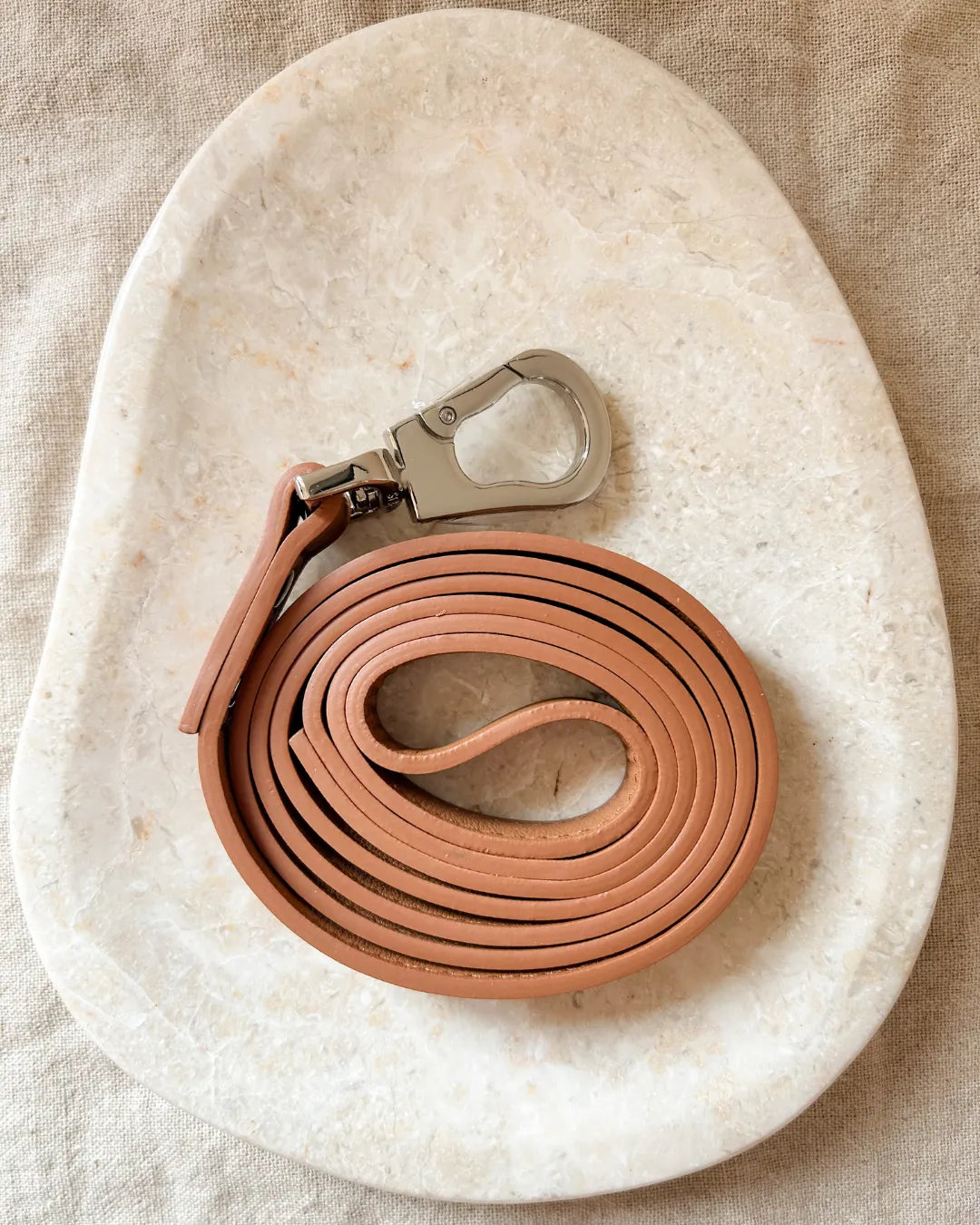Brown luxury vegan leather dog leash with silver clip on a beige stone surface