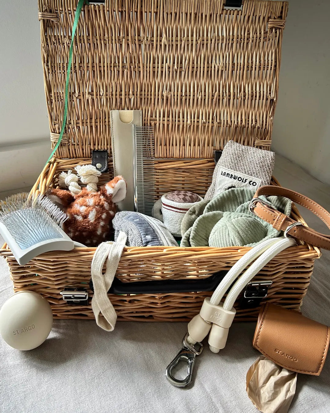 Wicker basket with luxury dog toys and accessories inside, all with a neutral background