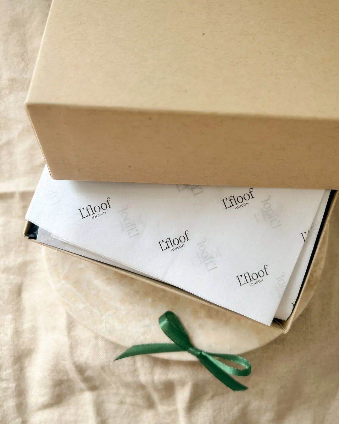 L'floof product packaging with a white box and green ribbon on a beige surface
