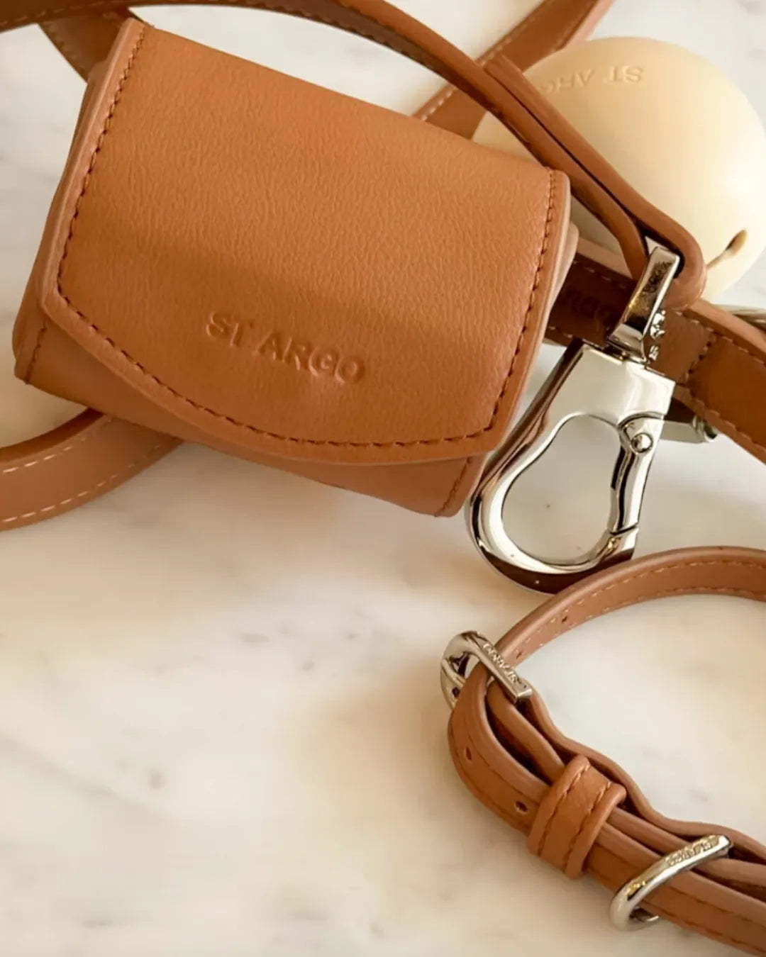 Close-up of a luxury brown vegan leather bag with 'ST. ARGO' branding on a marble surface.