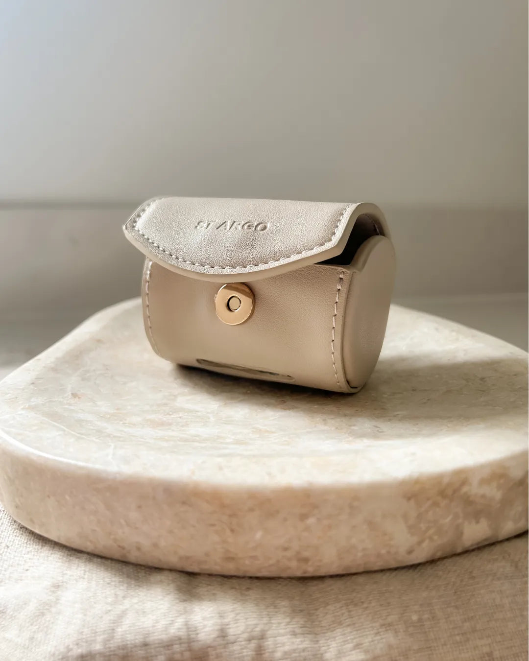 Beige vegan leather dog poop bag case with a gold button on a marble surface