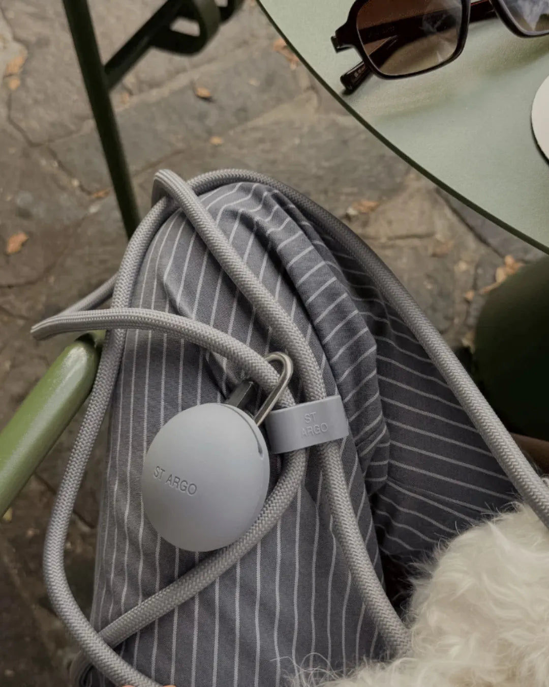 A grey, round luxury dog treat pouch with a grey rope on someone's lap