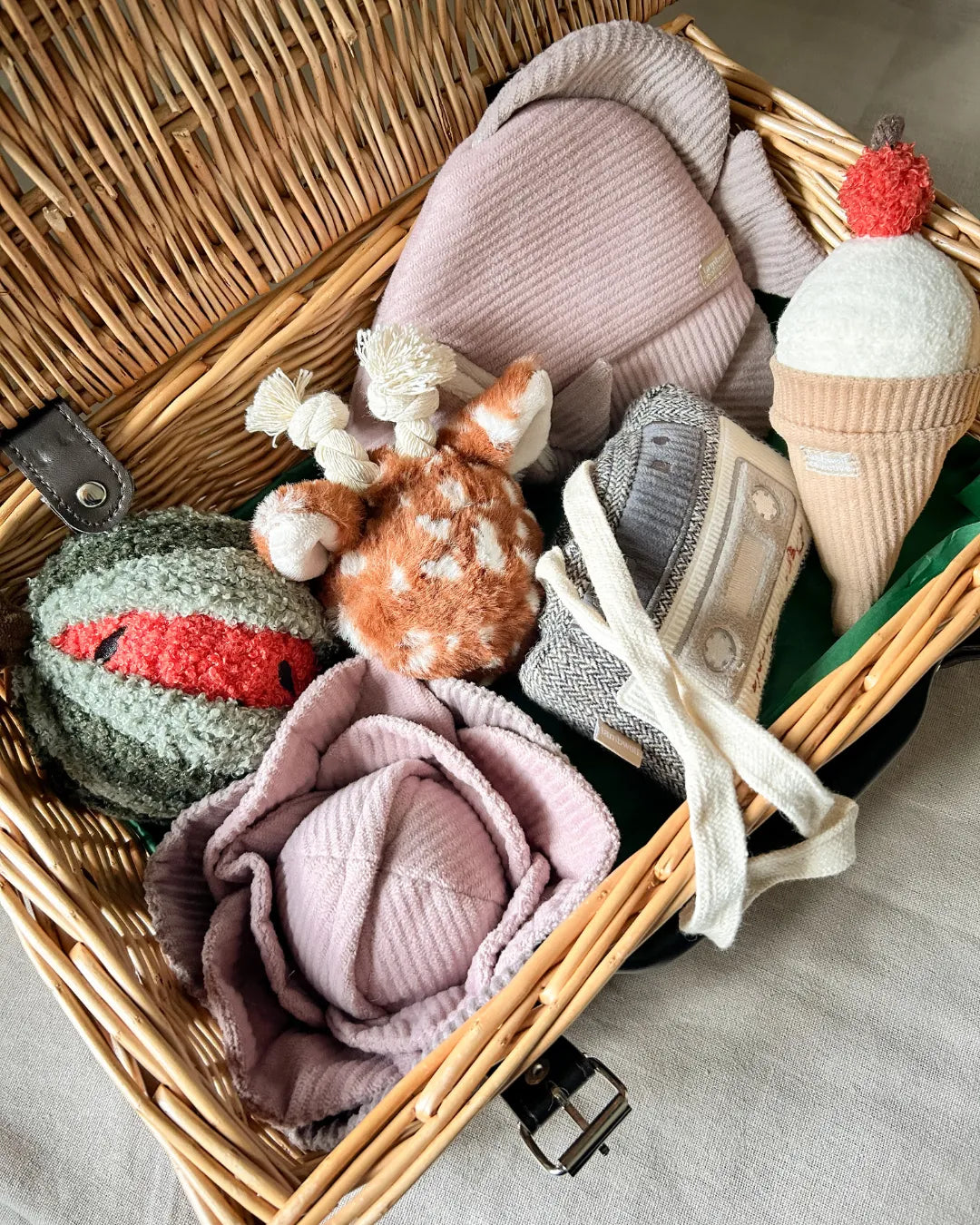 Luxury wicker hamper with plush dog toys including a pink fish toy, a green watermelon toy and a brown deer-like plush toy.