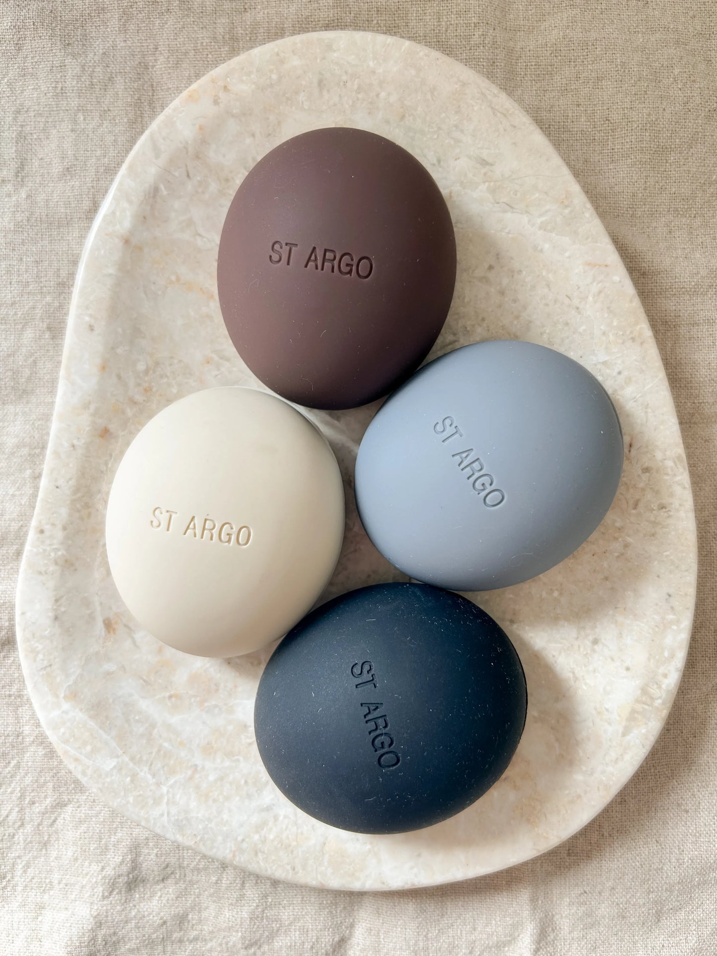 Neutral silicone luxury dog treat pouches in grey, black, cream, brown on a beige marble background