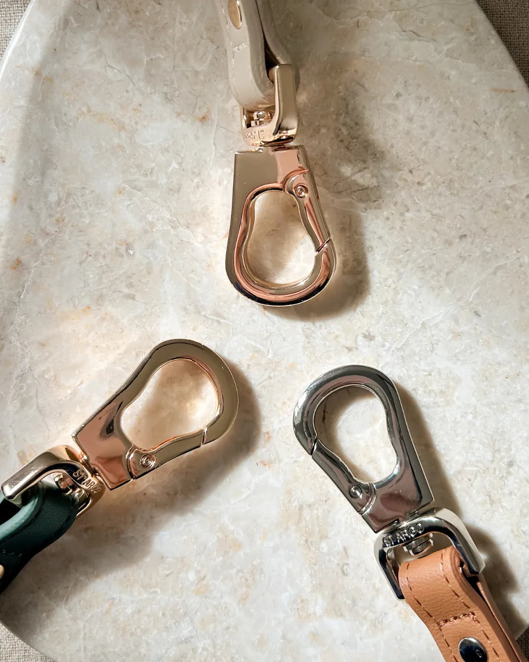Three metal carabiners on the end of luxury dog leads on a marble surface