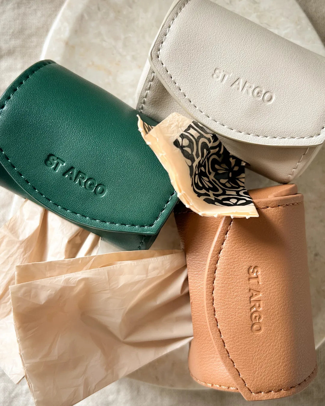 Three vegan leather dog poo bag holders in green, beige and brown with 'St. Argo' branding on a light background.
