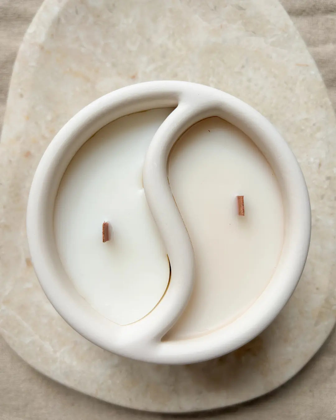 Yin and yang white candle in a ceramic holder on a beige surface