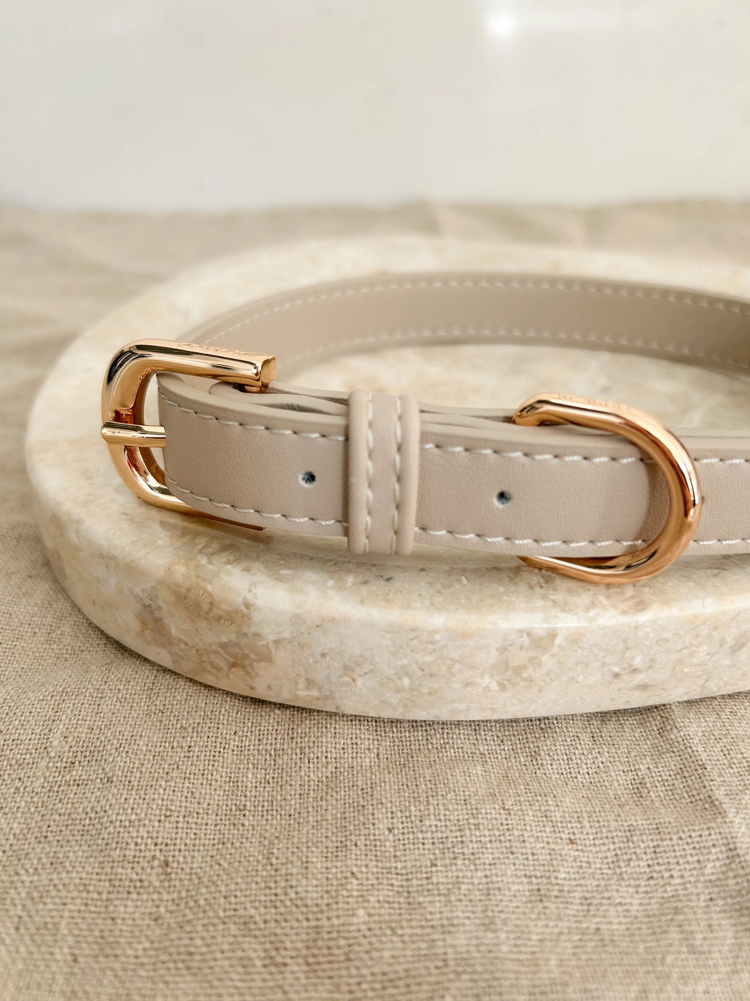 Beige luxury dog collar with gold hardware on marble stone and beige linen background