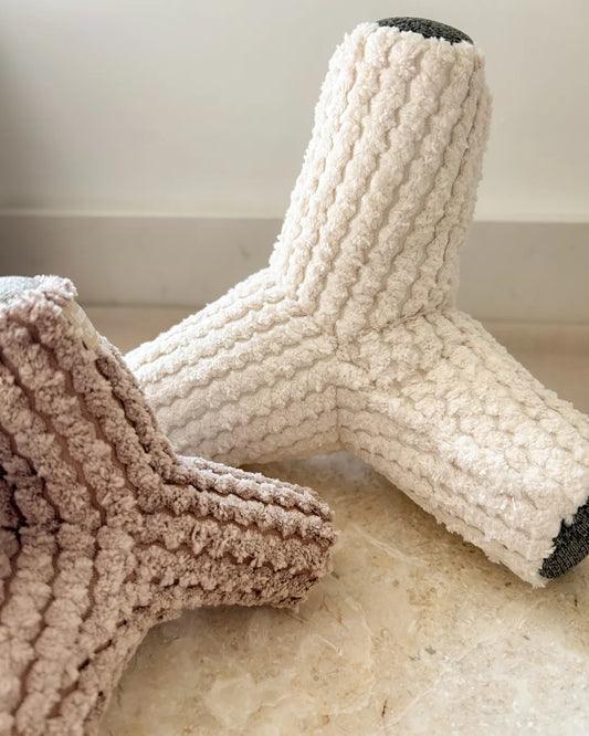 Textured beige and brown dog toys on a light marble floor.