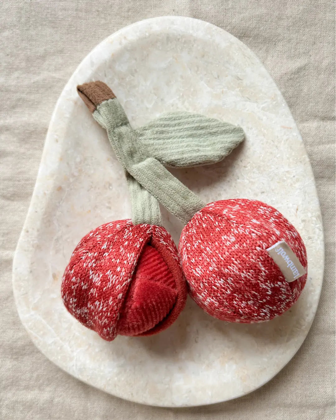 Plush cherry dog toy on a stone surface