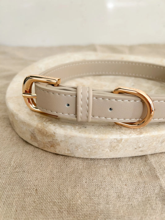 Beige luxury dog collar with gold hardware on a linen towel and beige marble.