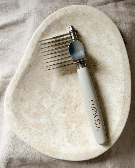 Pet grooming tool with 'Pupwell' branding on a marble surface