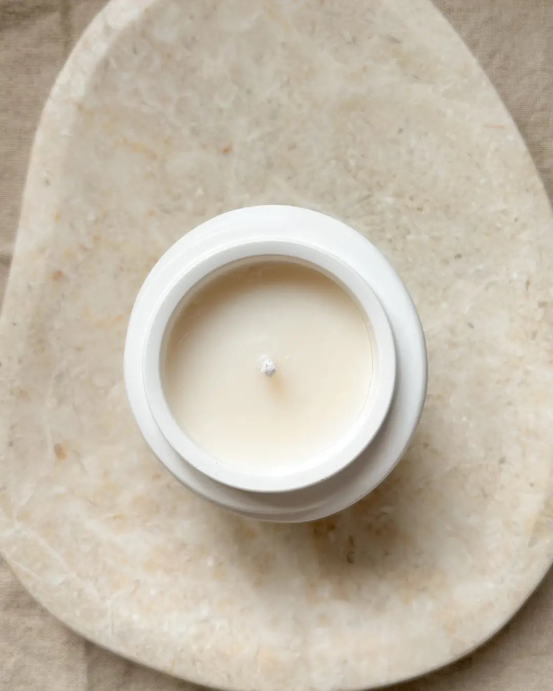 White candle in a ceramic holder on a beige stone surface