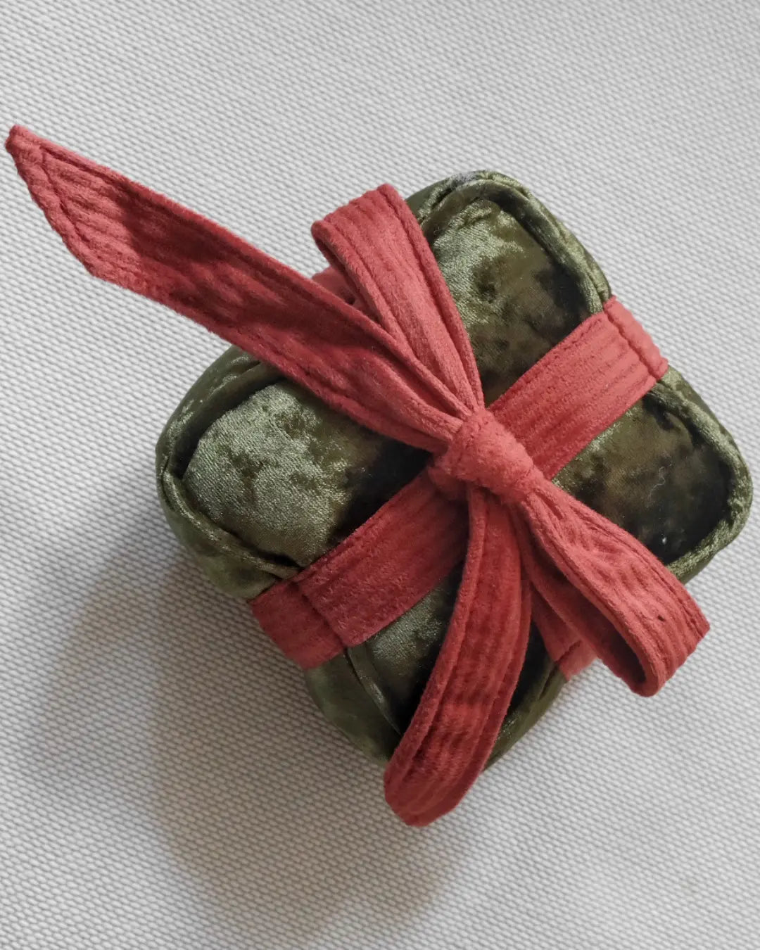 Green plush present-shaped dog toy with a red ribbon on a white background