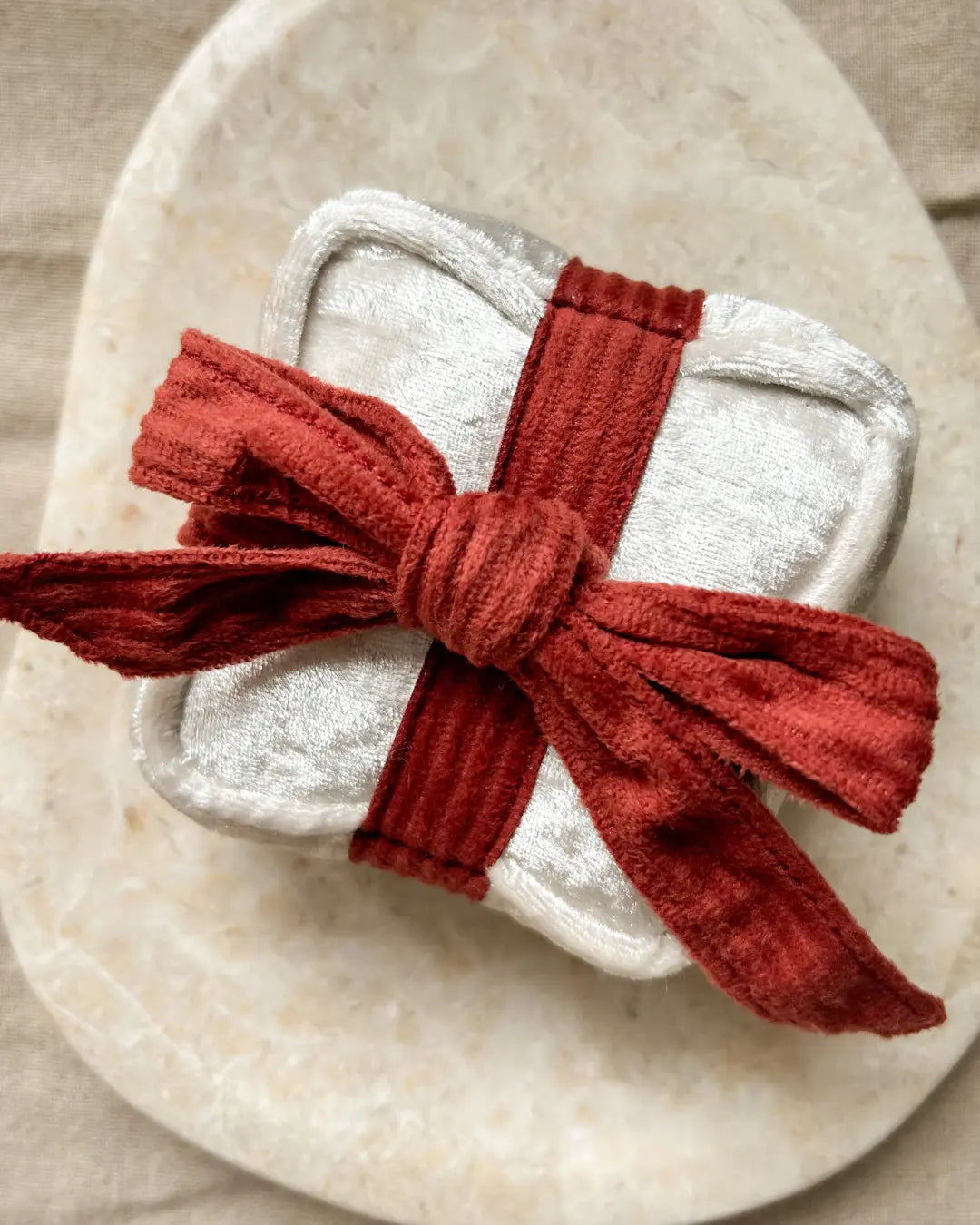 White gift-shaped dog toy tied with a red ribbon on a beige stone surface