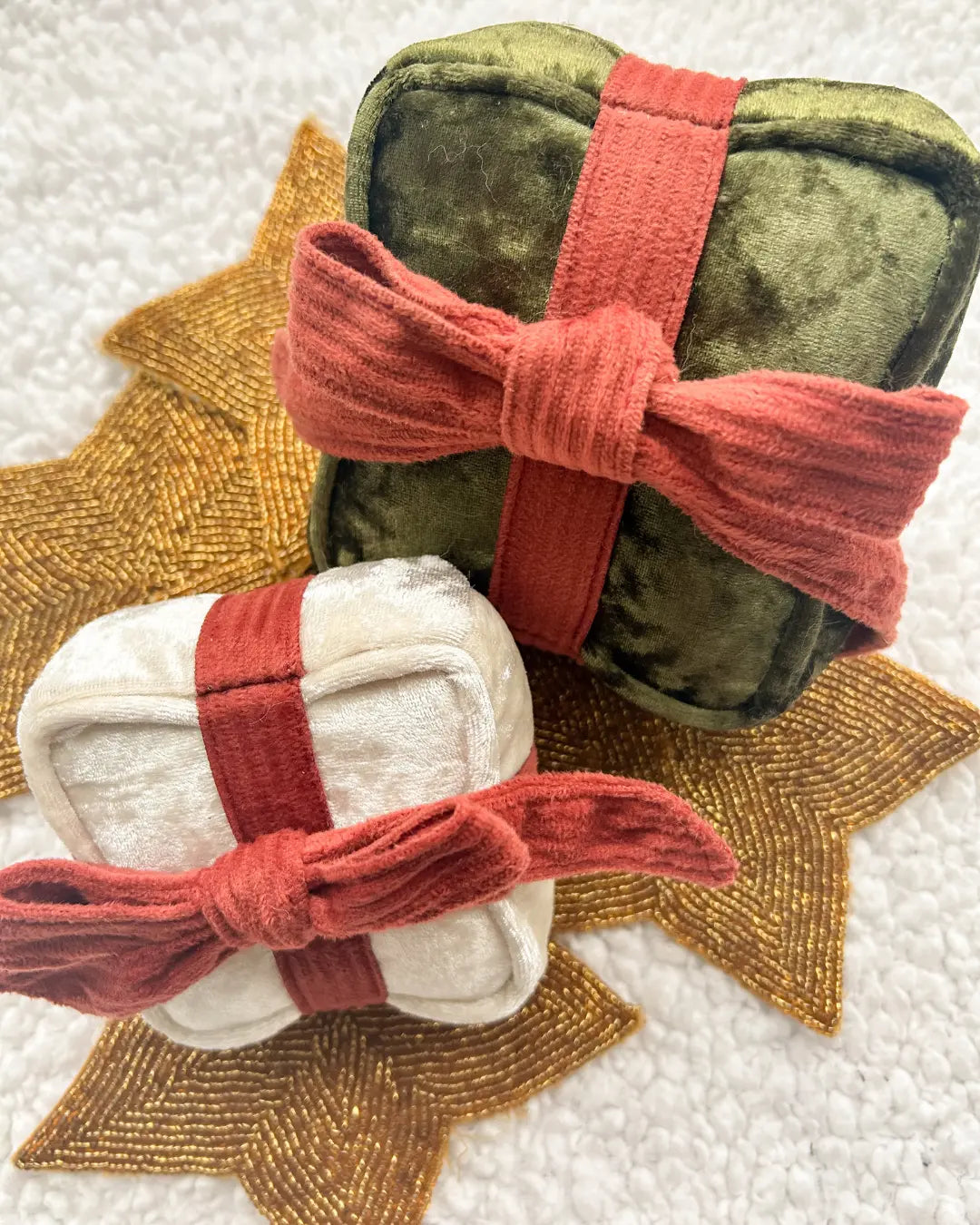 Two small wrapped present-shaped dog toys with red ribbons on a textured surface