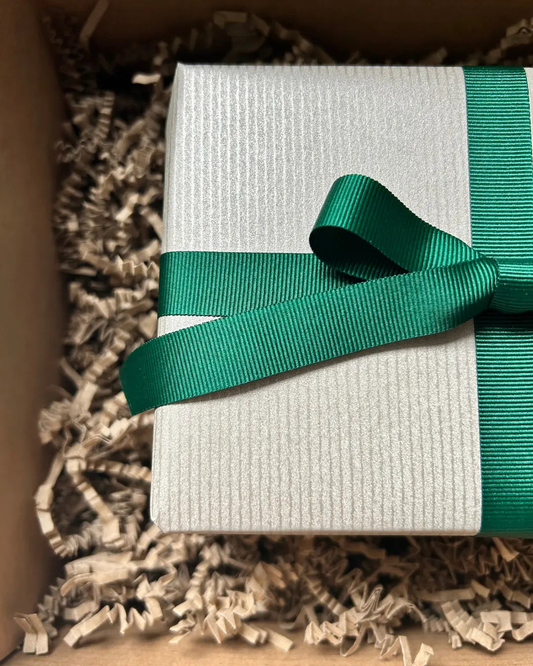 Light gold gift box with a green ribbon inside a box with crinkle paper