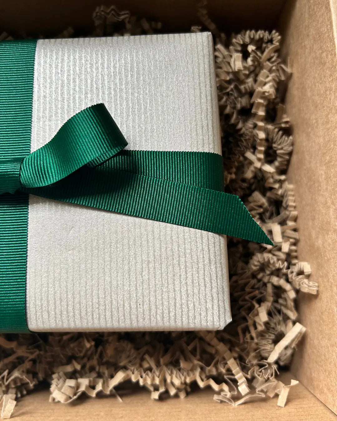 Light gold gift box with a green ribbon inside a brown box