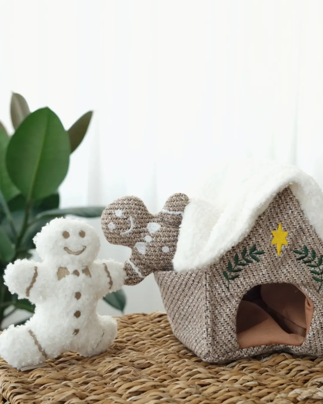 Gingerbread-themed dog snuffle toys including a gingerbread house and two gingerbread men on a textured surface with a blurred plant in the background.