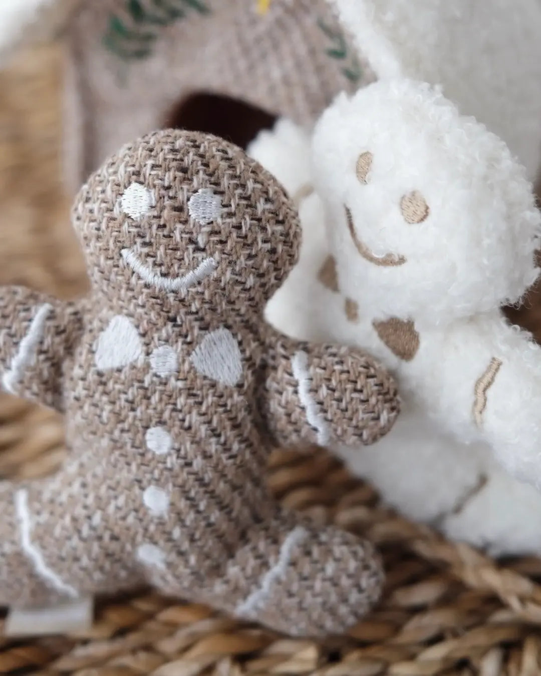 Textile dog toys shaped as gingerbread men in beige and white on a woven surface