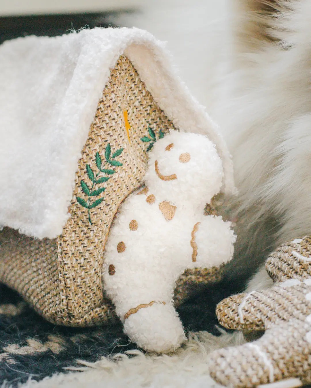 White plush gingerbread man dog toy and a crinkly gingerbread hous on a textured surface