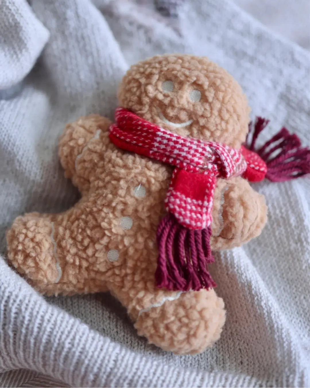 Gingerbread man dog toy with a red and white checkered scarf on a textured fabric background