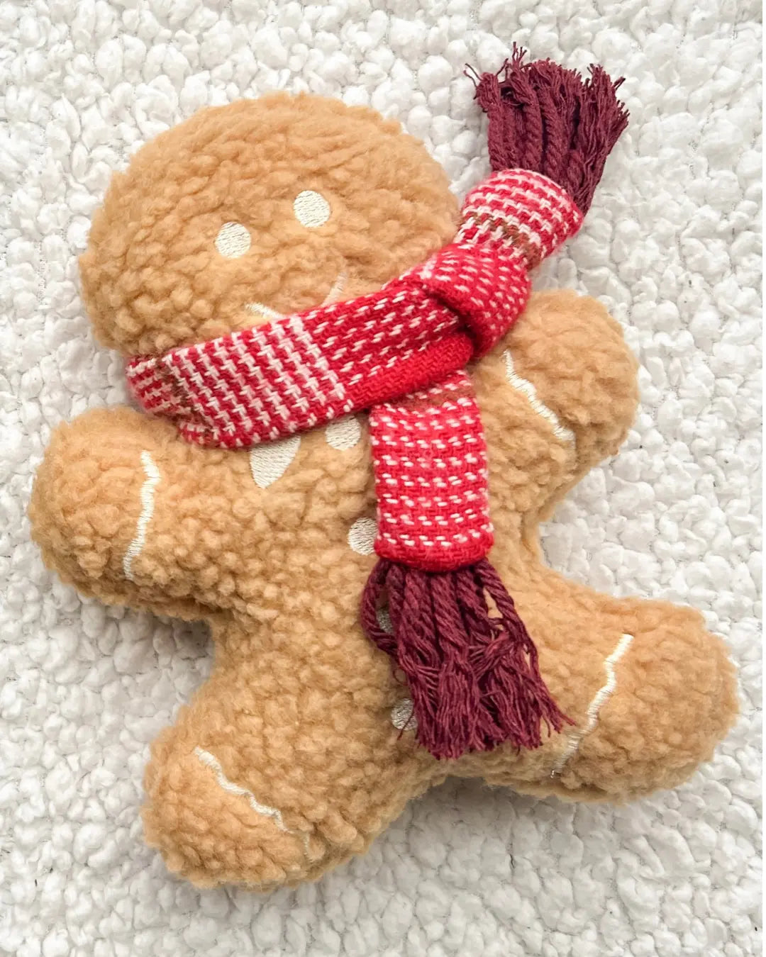 Gingerbread man plush toy with a red and white scarf on a textured white background