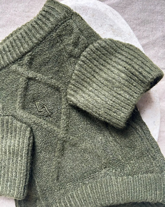 Close-up of a green knitted dog jumper with a brand logo on a white background
