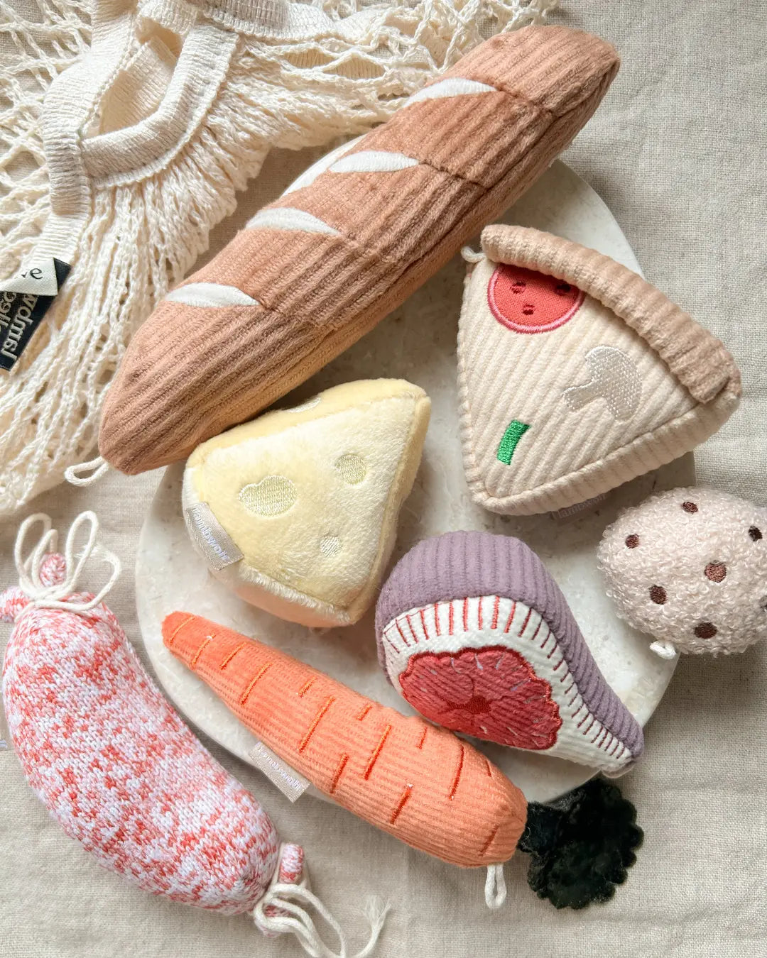 Set of soft dog toys in the shape of food items including a loaf of bread, cheese wedge, and vegetables on a textured surface