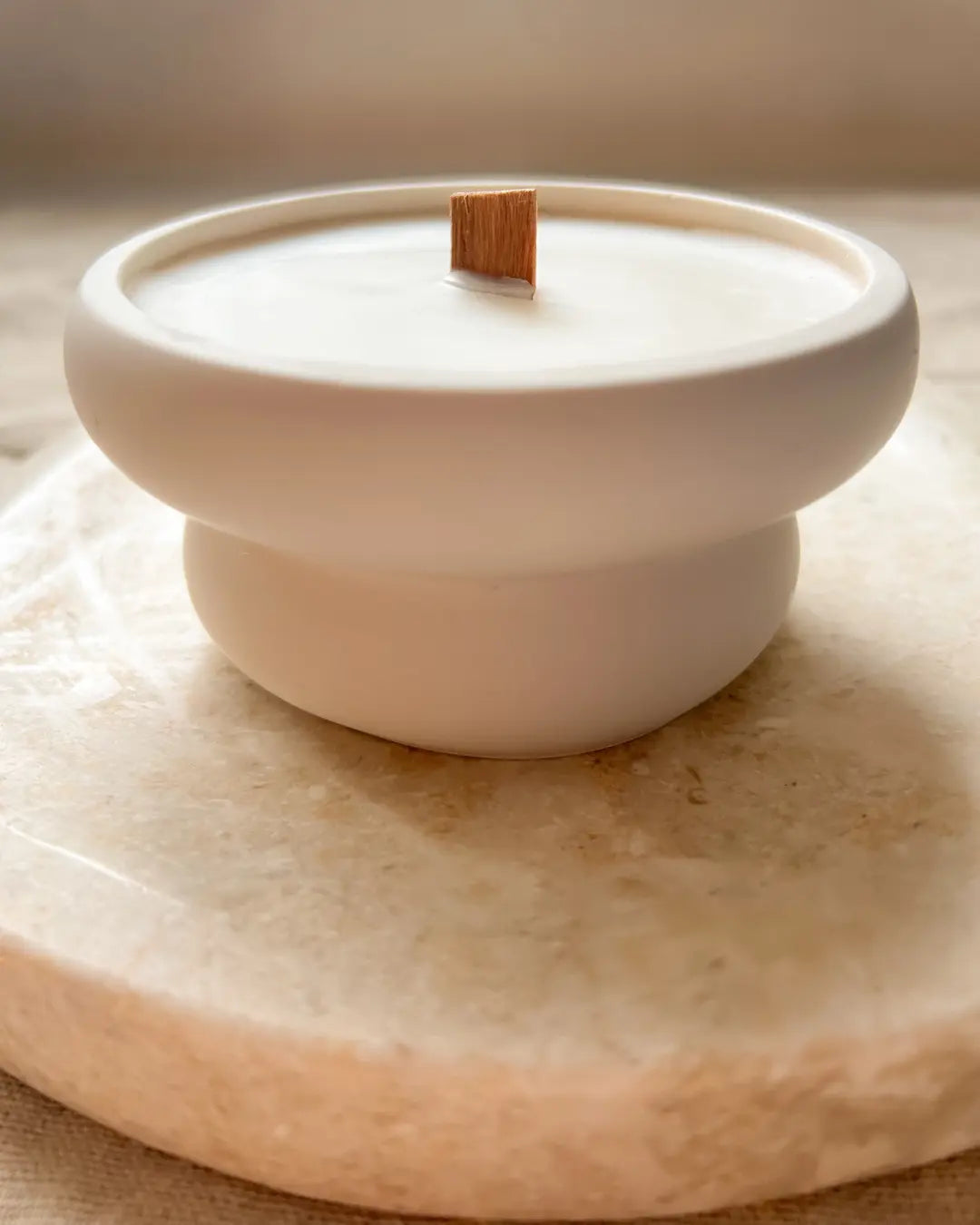 White ceramic candle holder with a wooden wick on a beige surface