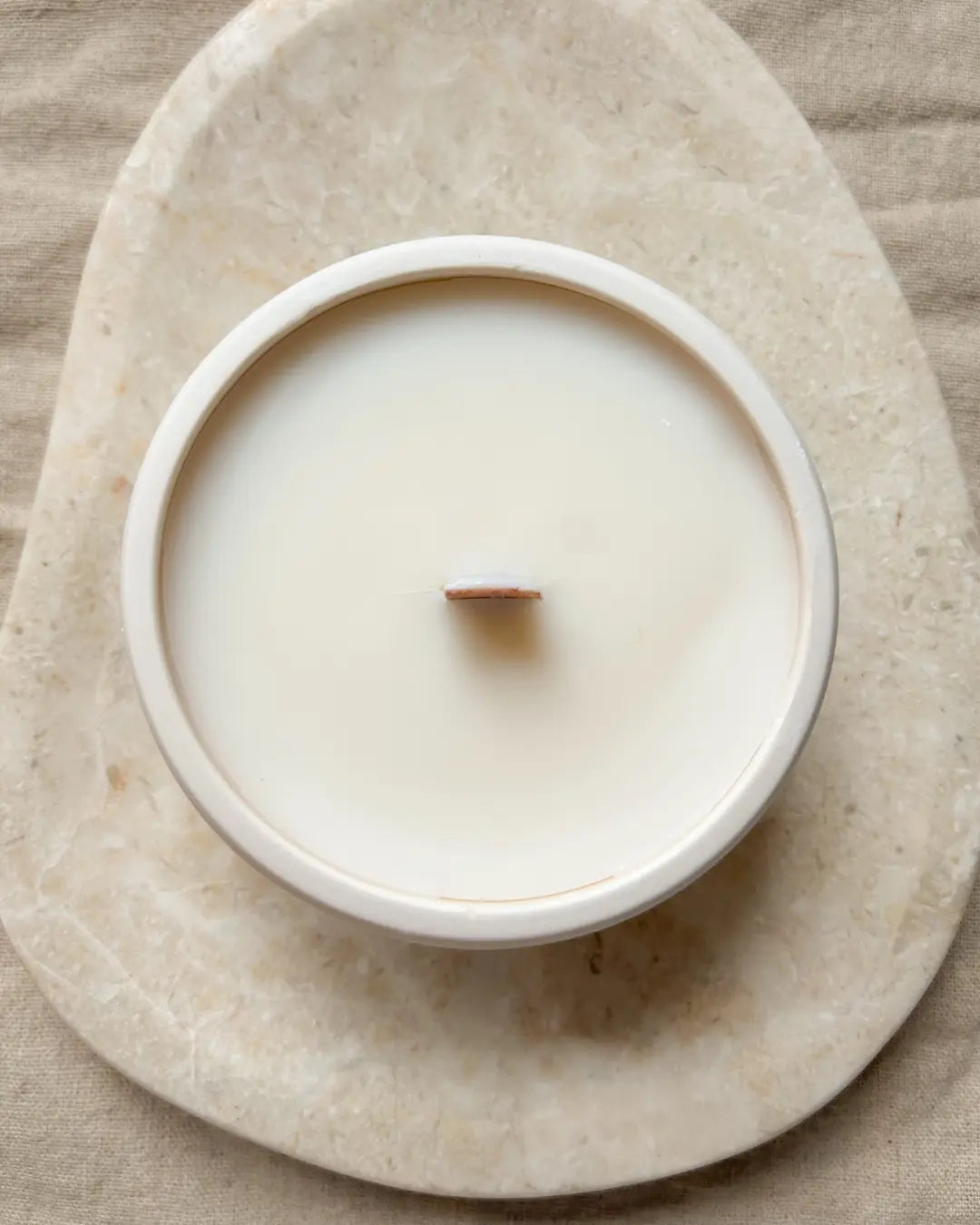 Candle in a white holder on a beige stone surface