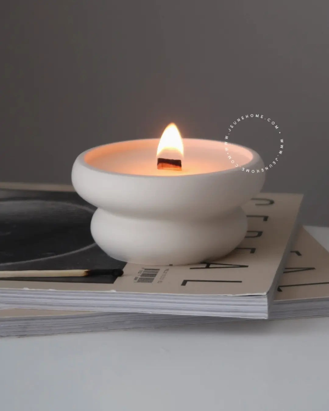 White ceramic candle holder with a lit candle on top of a magazine
