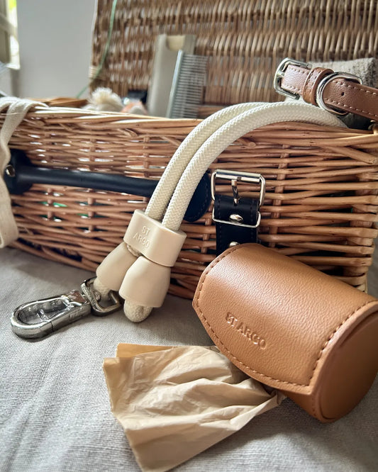 Close-up of a vegan leather dog poo bag holder and a rope handsfree lead with a luxury wicker hamper in the background