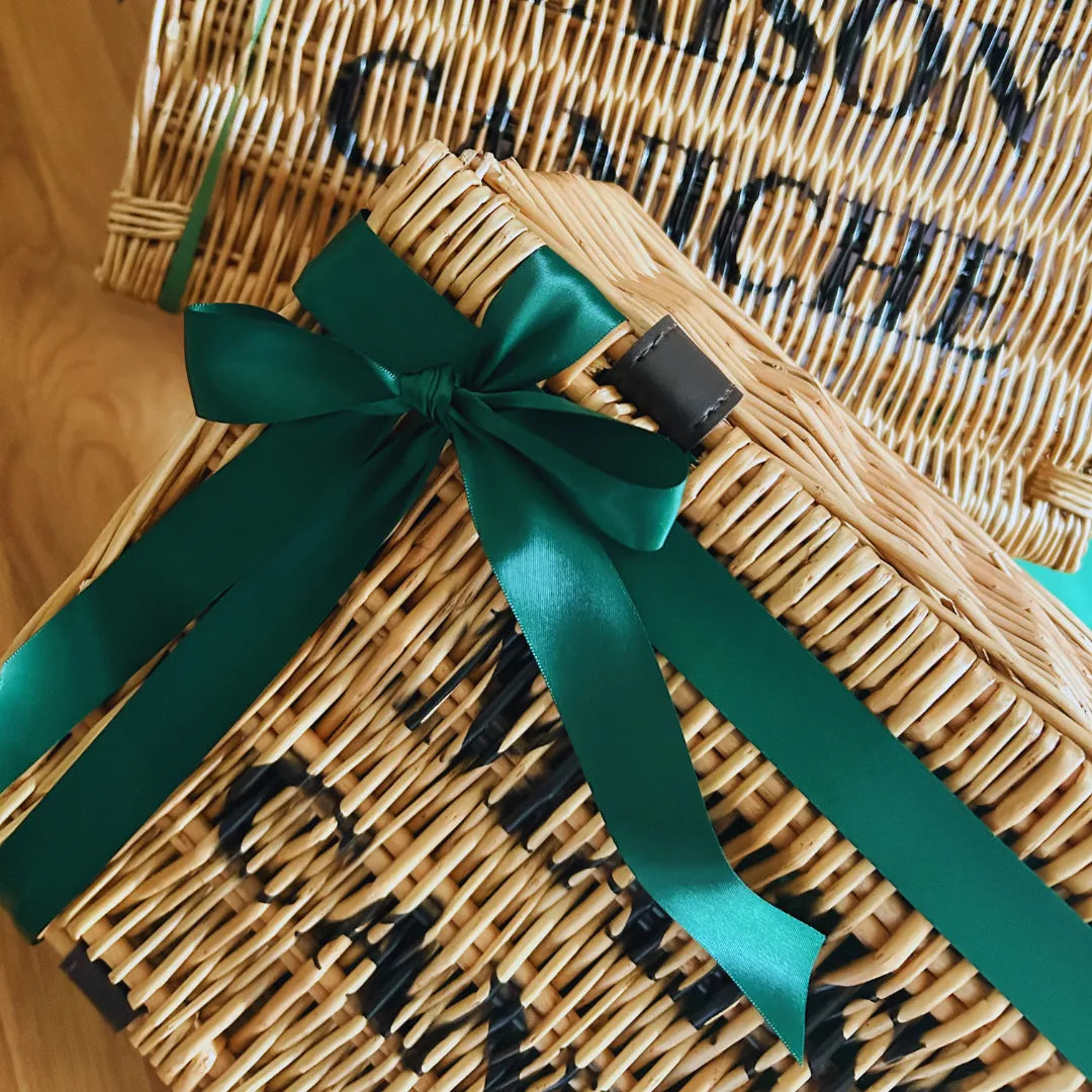Wicker hamper with a green ribbon on a wooden surface
