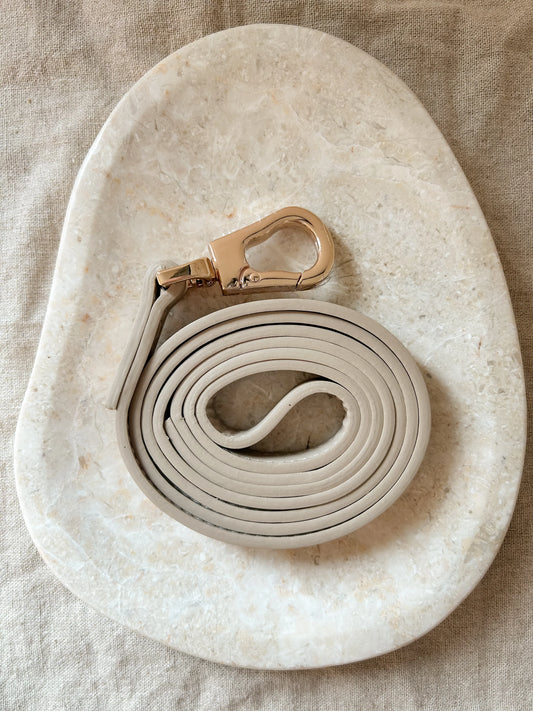 Luxury vegan leather dog lead with gold hardware on a beige marble and linen background