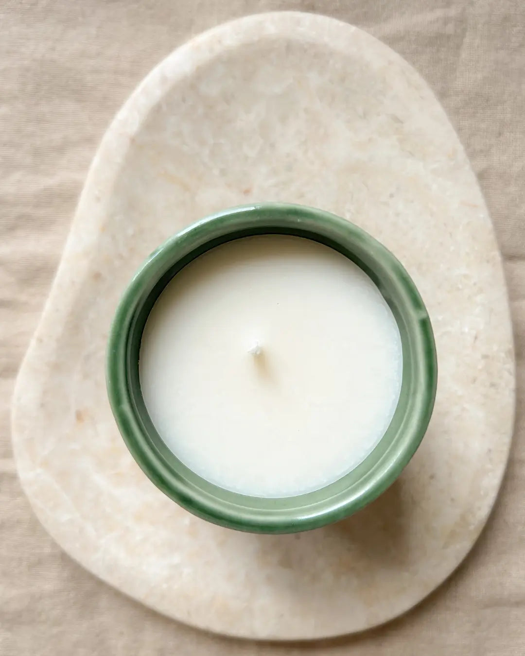 Candle in a green container on a stone surface