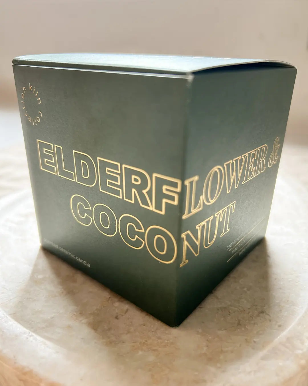 Green candle box with 'Elderflower & Coconut' text on a marble surface