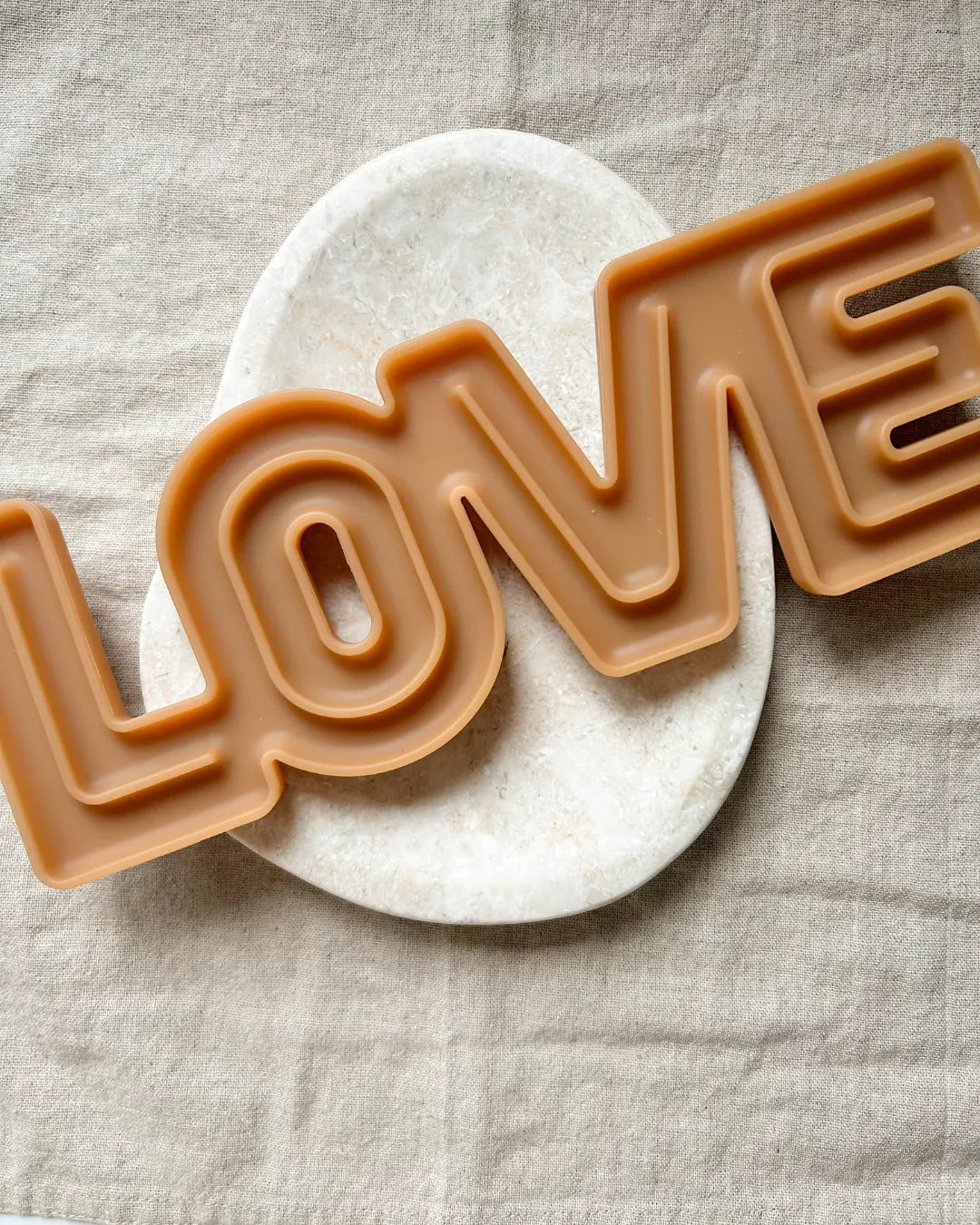 Brown 'LOVE' letter-shaped dog lick mat on a beige fabric background